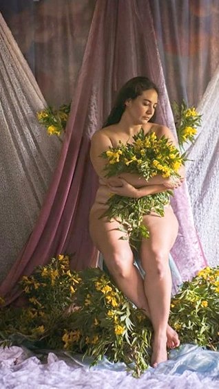 Alejandra Porta seated among draped fabric, holding yellow flowers