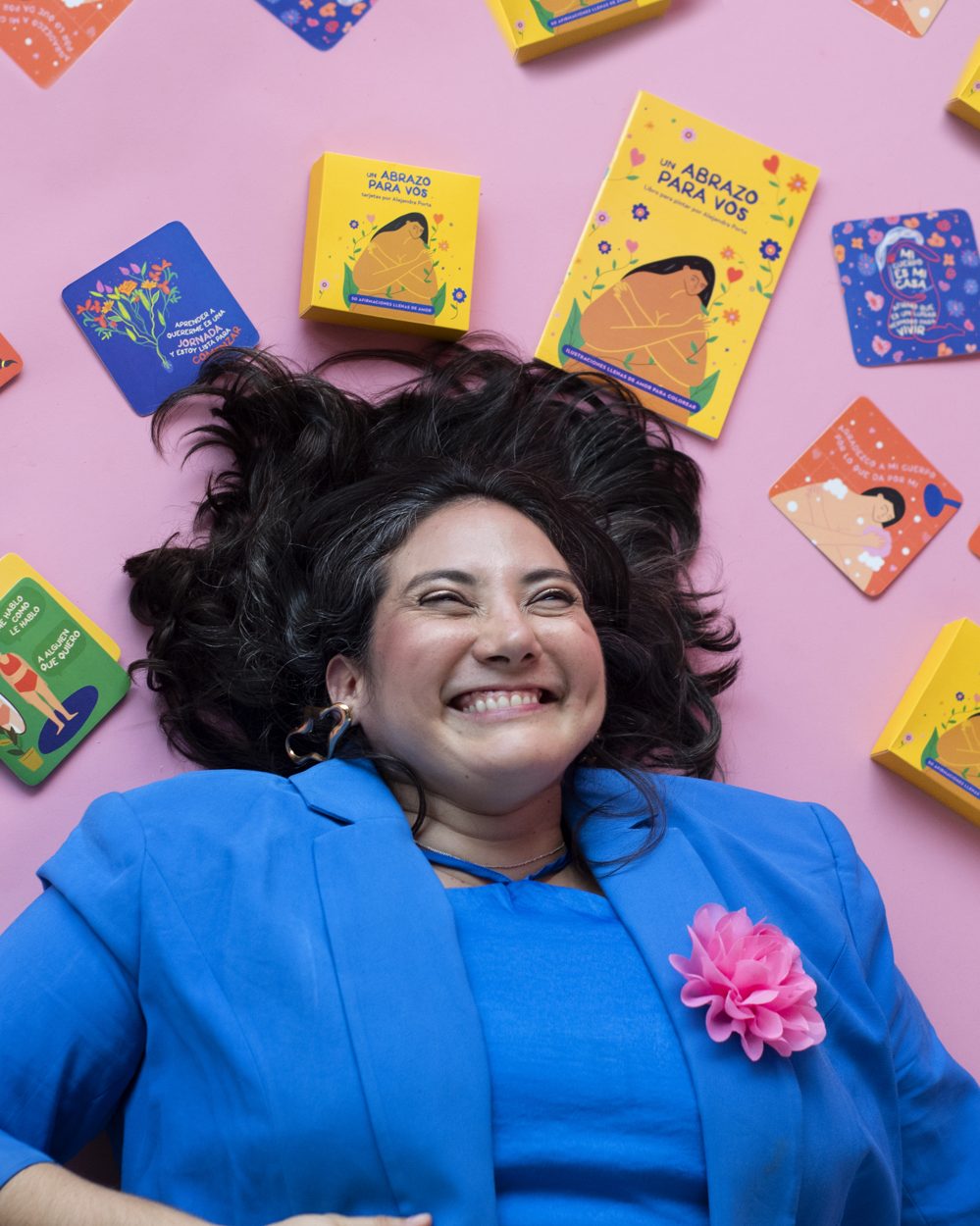 Ale laughing on a pink floor surrounded by her affirmation cards and coloring book