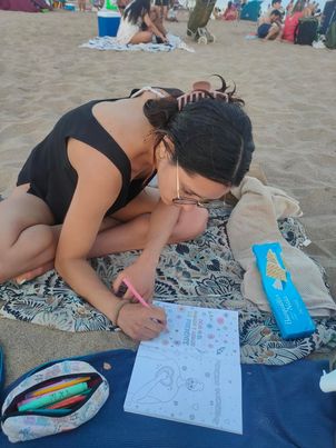 A woman coloring Ale's coloring book on a towel at the beach
