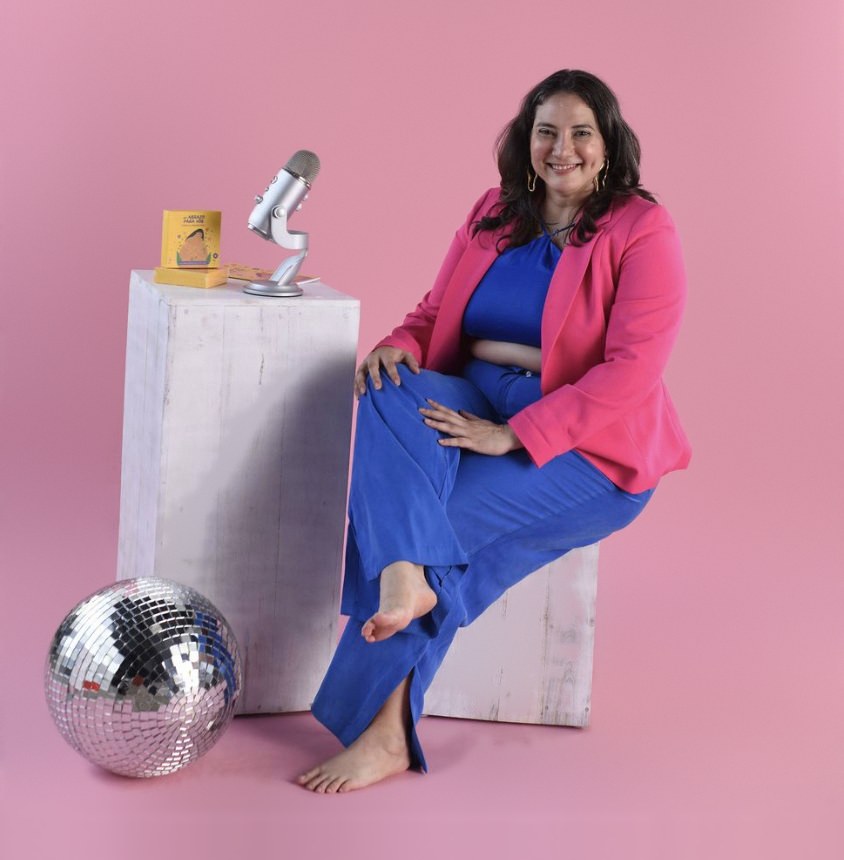 Ale smiling, seated next to a podcast microphone and her affirmation cards